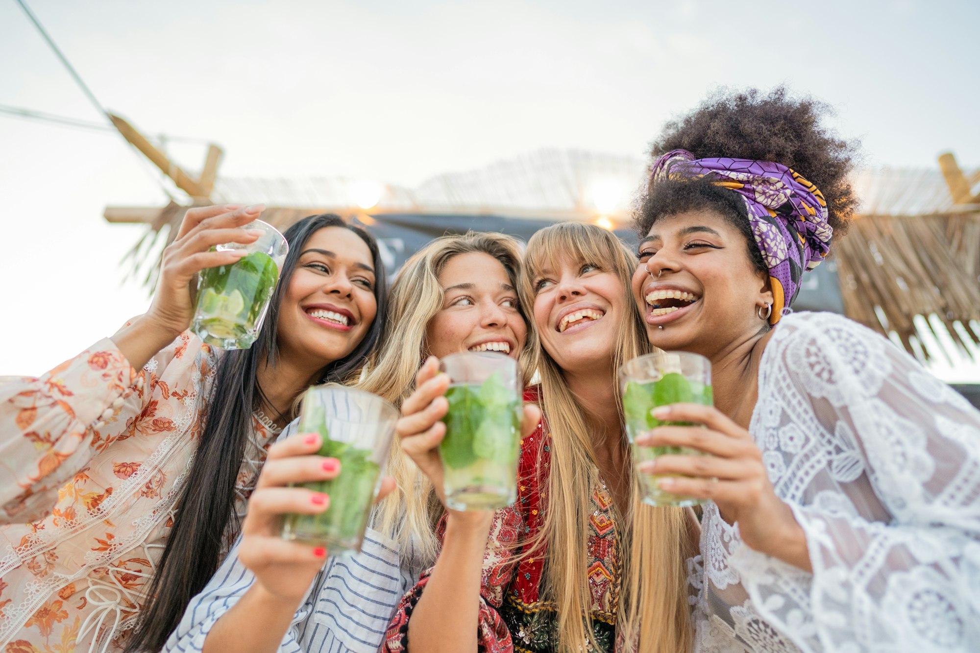 Cheerful girls having fun and toasting mojito at bar on the beach.